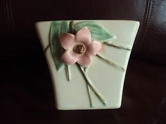 a ceramic vase with a pink flower and green leaves on the top, sitting on a leather couch