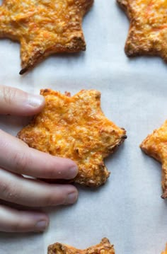 someone reaching for some cheesy food on a sheet of parchment paper with their hand