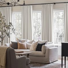 a living room filled with furniture and lots of windows covered in white drapes