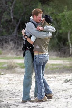 two people hugging each other in the sand with trees in the back ground behind them