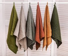 four towels hanging on a rack in front of a window with shutters and blinds