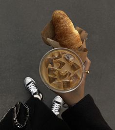 a person holding up a drink with ice and croissants