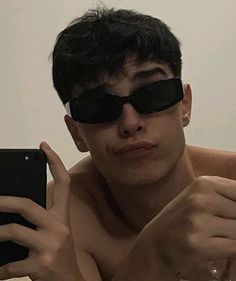 a shirtless man wearing sunglasses taking a selfie with his cell phone