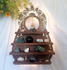 a wooden shelf with various items on it and a mirror in the middle, surrounded by greenery