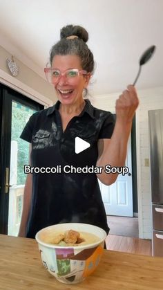 a woman holding a spoon in her right hand while standing next to a bowl of food