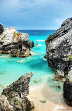 the beach is surrounded by large rocks and clear blue water