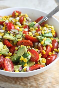 a white bowl filled with corn, tomatoes and avocado salad on top of a wooden cutting board