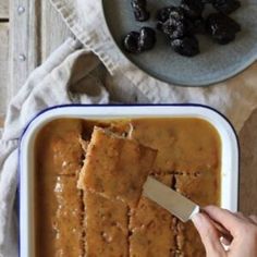 a person is cutting into some food in a dish with olives on the side