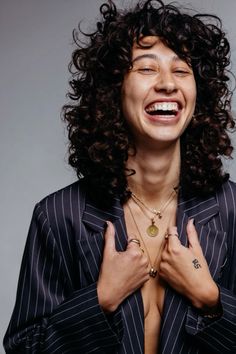 a woman with curly hair wearing a suit and holding her hands together in front of her chest