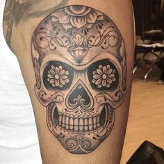 a man's arm with a skull tattoo on it and flowers in the middle