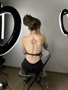 a woman is sitting in a chair with her back turned to the camera and has a star tattoo on her upper back