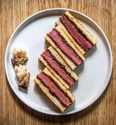 a white plate topped with cut in half sandwiches next to crackers and cauliflower