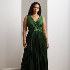 a woman in a long green dress stands against a white wall and looks off to the side