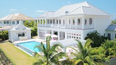 an aerial view of a large white house with a pool in the foreground and palm trees surrounding it