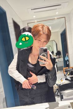 a woman taking a selfie in front of a mirror with an alien mask on her head