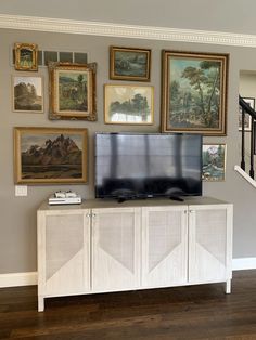 a flat screen tv sitting on top of a white cabinet in a living room next to stairs