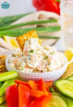 a white bowl filled with dip surrounded by vegetables and crackers