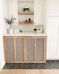 a kitchen with white cabinets and wood flooring in the center is an open shelving unit that has wicker doors on both sides