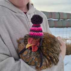 a woman holding a chicken wearing a knitted hat