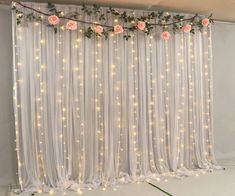 the room is decorated with white curtains and pink flowers on them, along with fairy lights