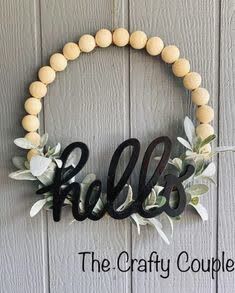 a wreath with the word hello painted on it and some wood beads hanging from it