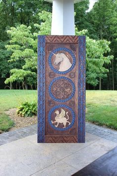 a wooden sign with horses on it in front of some trees and bushes, near a stone walkway