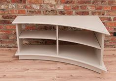 a white curved shelf sitting on top of a wooden floor next to a brick wall