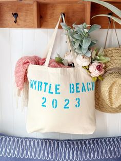 a tote bag hanging on the wall next to a hat and flowers in a basket