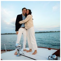 a man and woman standing on the back of a boat in front of some water