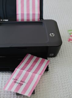 a printer sitting on top of a bed next to a pink and white striped paper