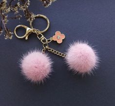 two pink pom poms hanging from a gold keychain on a blue surface