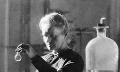 a black and white photo of a woman working in a glass factory with bottles behind her