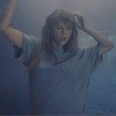 a woman standing in front of a blue wall with her hands on her head and arms behind her head