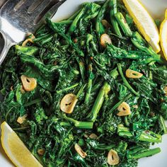 a white plate topped with green vegetables and lemon wedges next to a silver fork