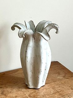 a white vase sitting on top of a wooden table next to a plant in it