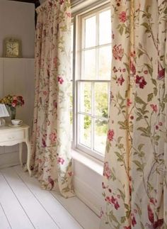 a bedroom with floral curtains and a white desk in front of a window that has a mirror on it