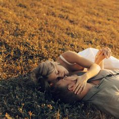 a man and woman laying on the ground in an open grassy field with their heads touching each other