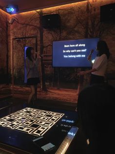 two women are standing in front of a screen with a video on it and one is holding a microphone