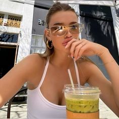 a woman wearing glasses sitting at a table with a drink in front of her face