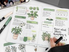 a person is holding a pen and looking at a planner with plants on it, next to a laptop