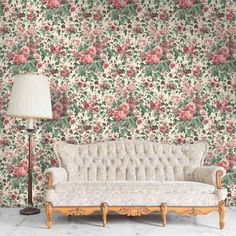 a white couch sitting next to a lamp on top of a wooden table in front of a floral wallpaper