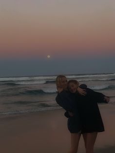 two women hugging each other on the beach at sunset with waves coming in and setting sun behind them