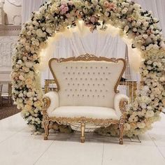 a white couch sitting under a flower covered arch in front of a chair with flowers on it