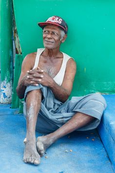 an old man sitting on the ground in front of a green wall