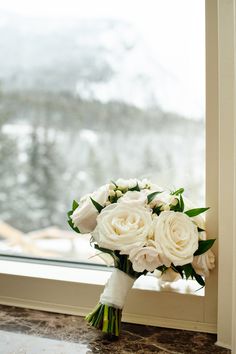 a bouquet of white roses sitting on top of a window sill next to a snow covered mountain