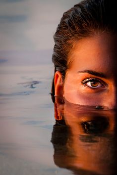 a woman's face is reflected in the water with her eyes wide open,