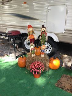 two scarecrows sitting on hay next to pumpkins in front of a camper