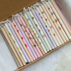 a box filled with different colored candles on top of a white table covered in paper