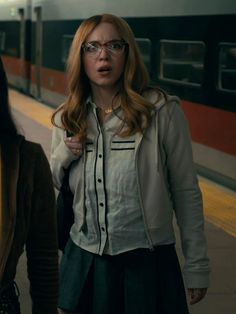 a woman with glasses standing next to a train at a station in front of another woman