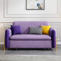 a purple couch sitting in front of a white wall with paintings on the wall behind it